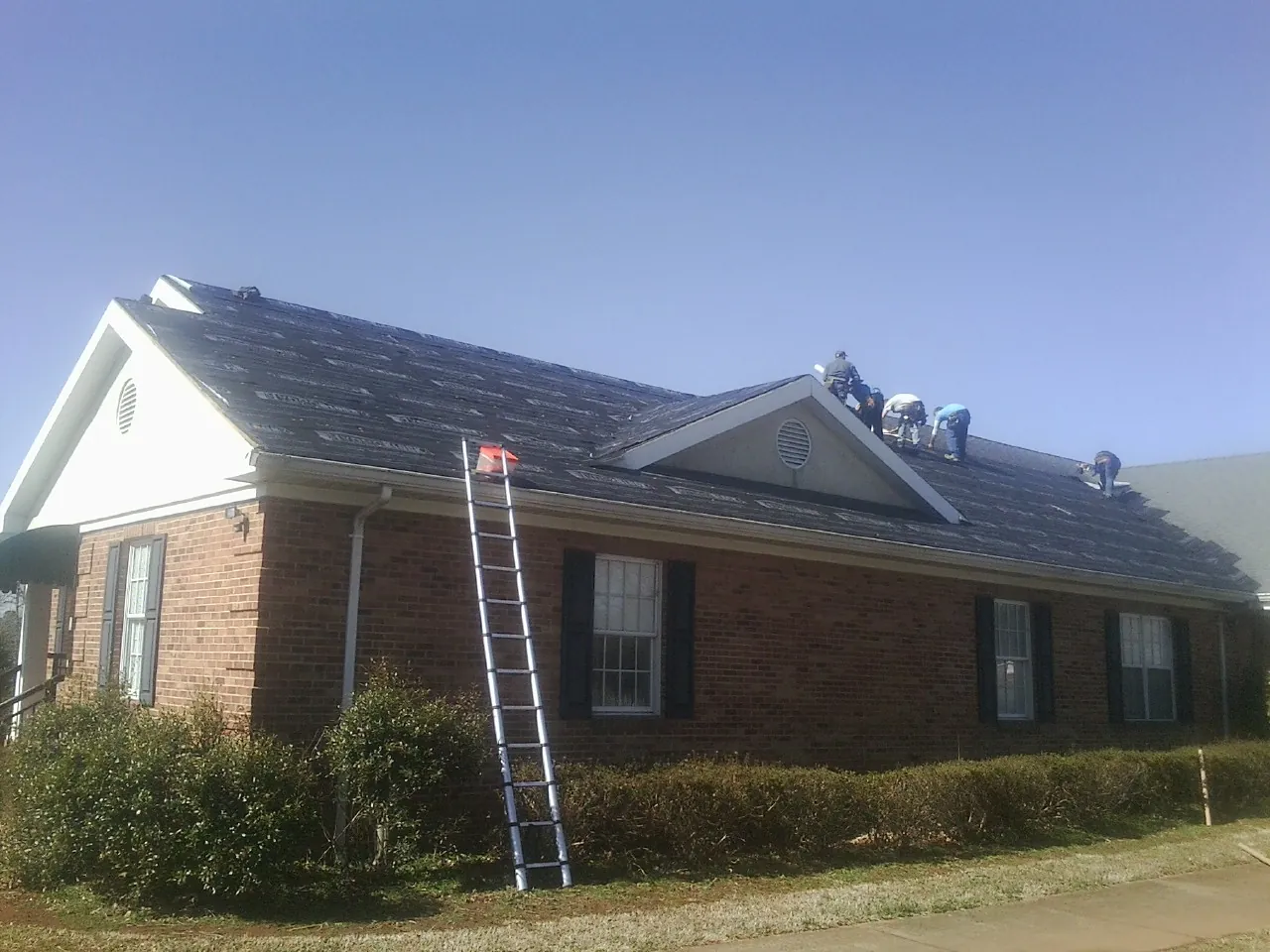 Crew tearing shingles off a brick ranch roof with a ladder set — Metal Roof Repair work by our crew in Woodstock